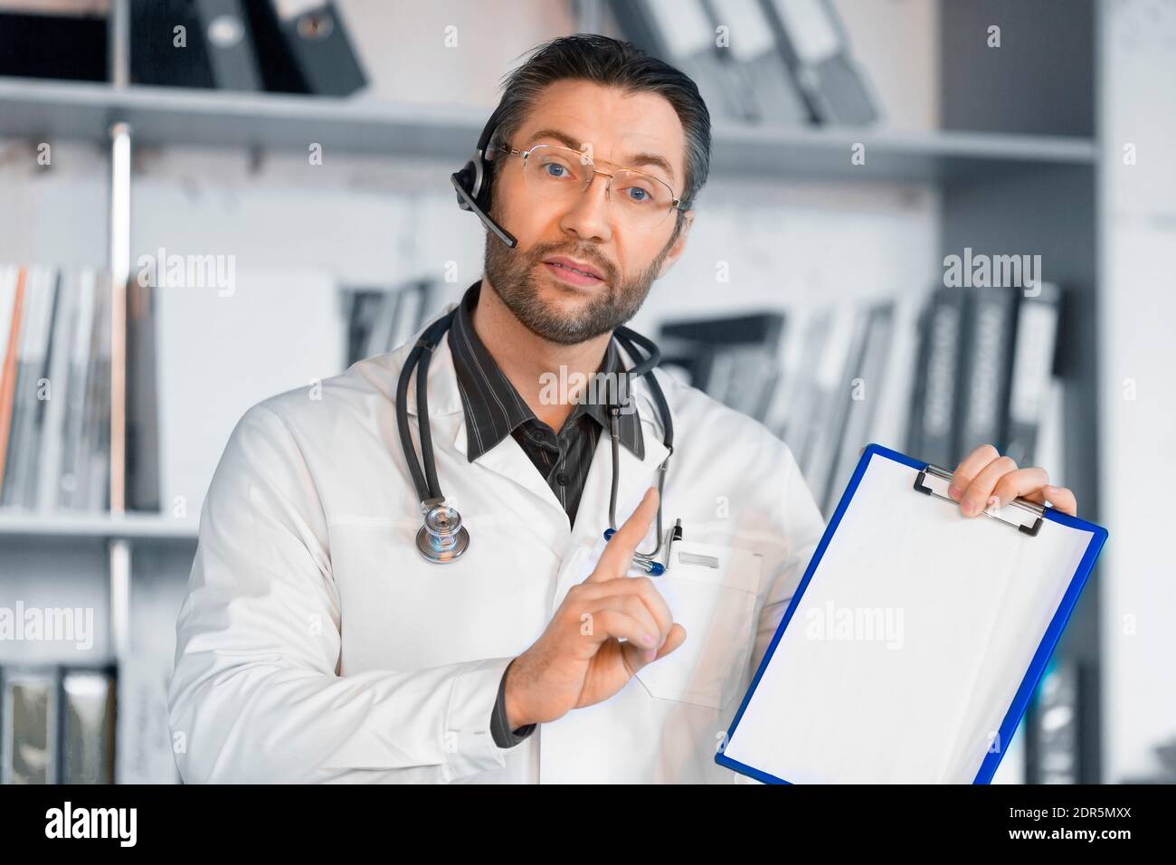 Dottore con cuffia dà consigli online e mostra i risultati su una clipboard. Concetto medico. Foto Stock