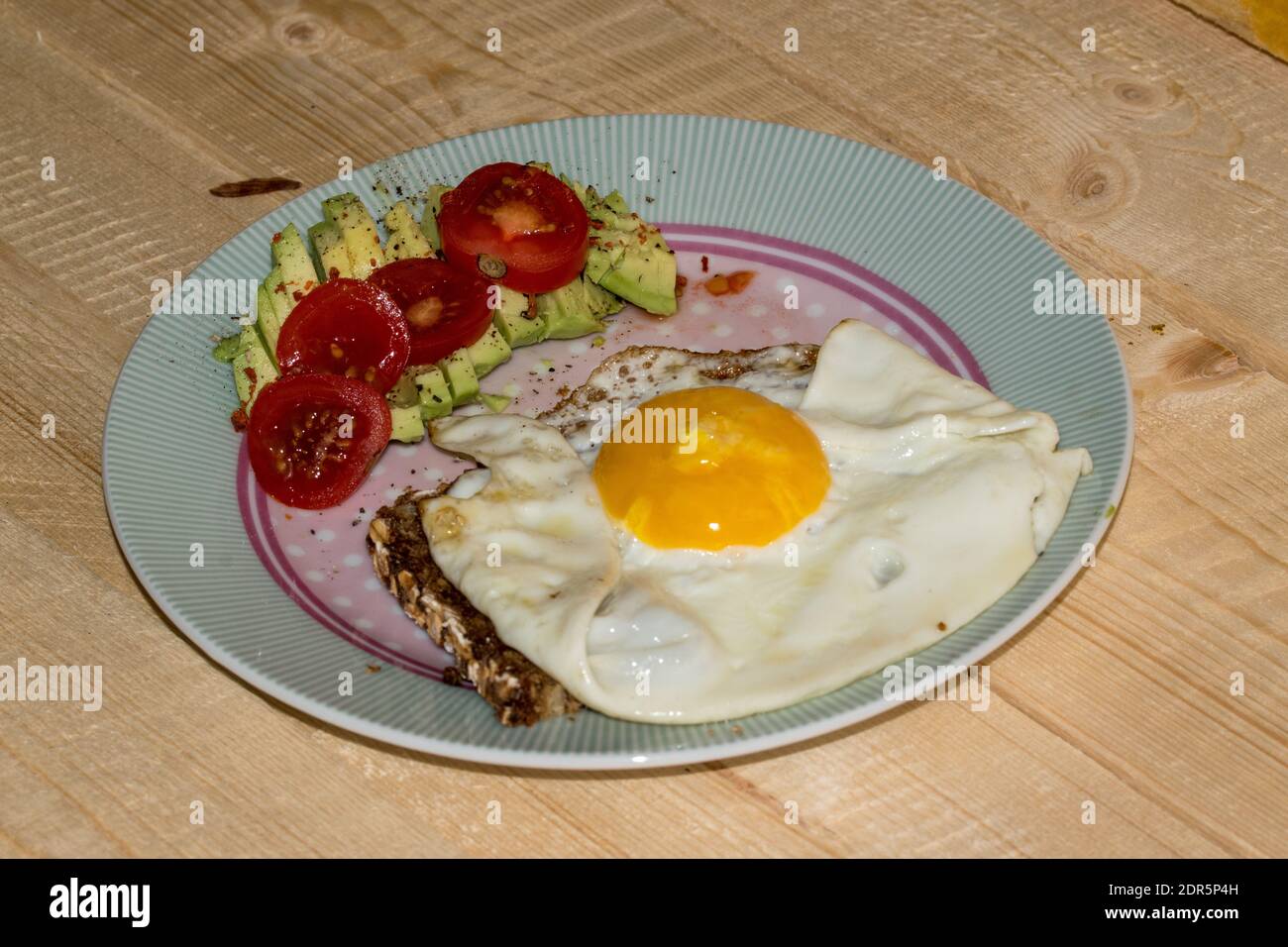 Uovo fritto su pane integrale con avocado a fette e pomodoro disposto su un piatto. Foto Stock