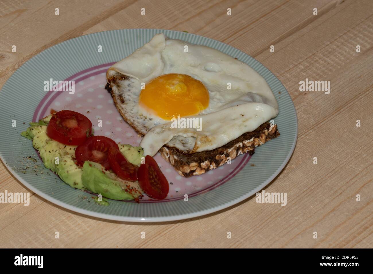 Uovo fritto su pane integrale con avocado a fette e pomodoro disposto su un piatto. Foto Stock
