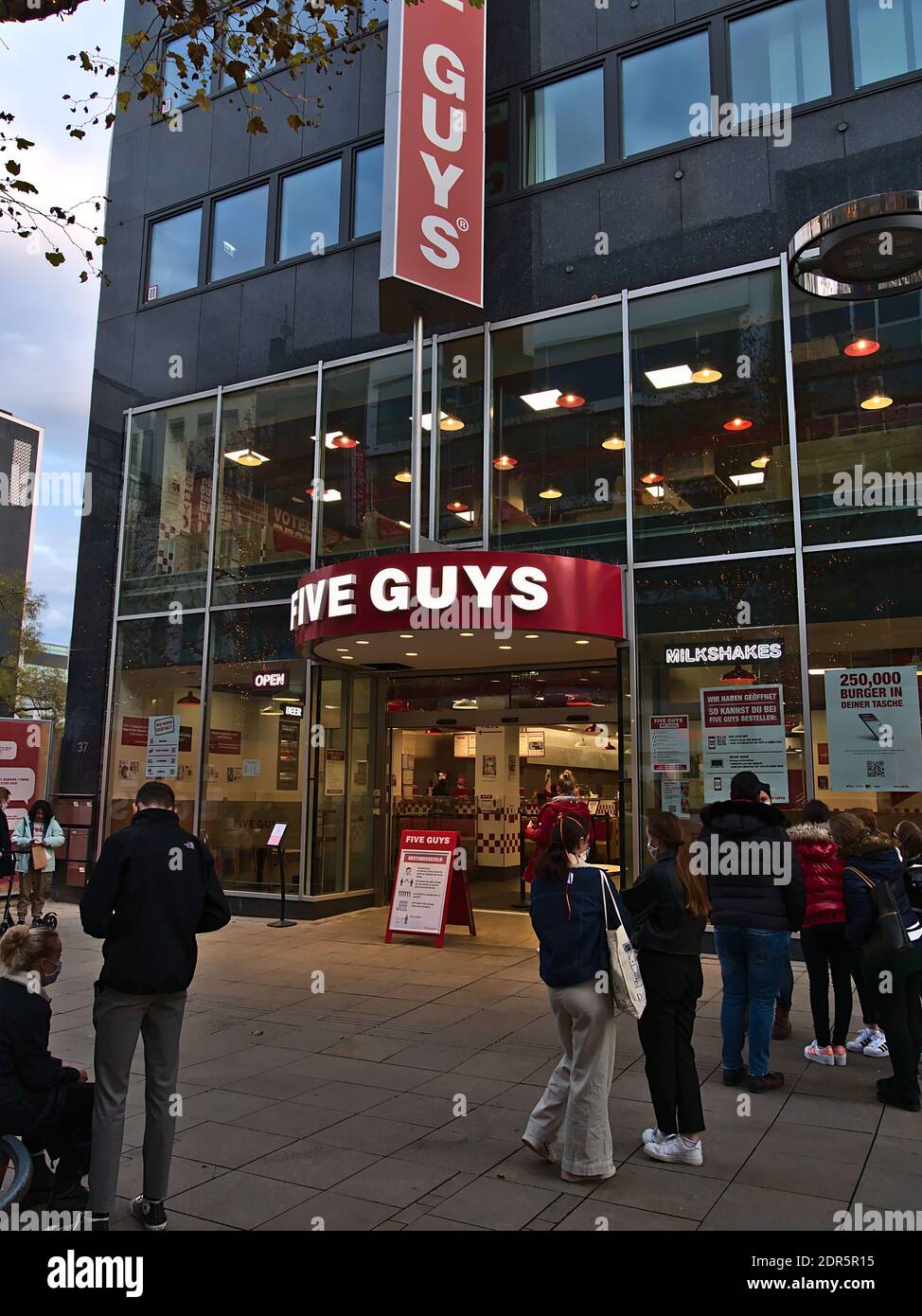 Persone che indossano maschere in attesa di raccogliere cibo pre-ordinato di fronte al recentemente aperto Burger ristorante Five Guys in via dello shopping Königstraße. Foto Stock