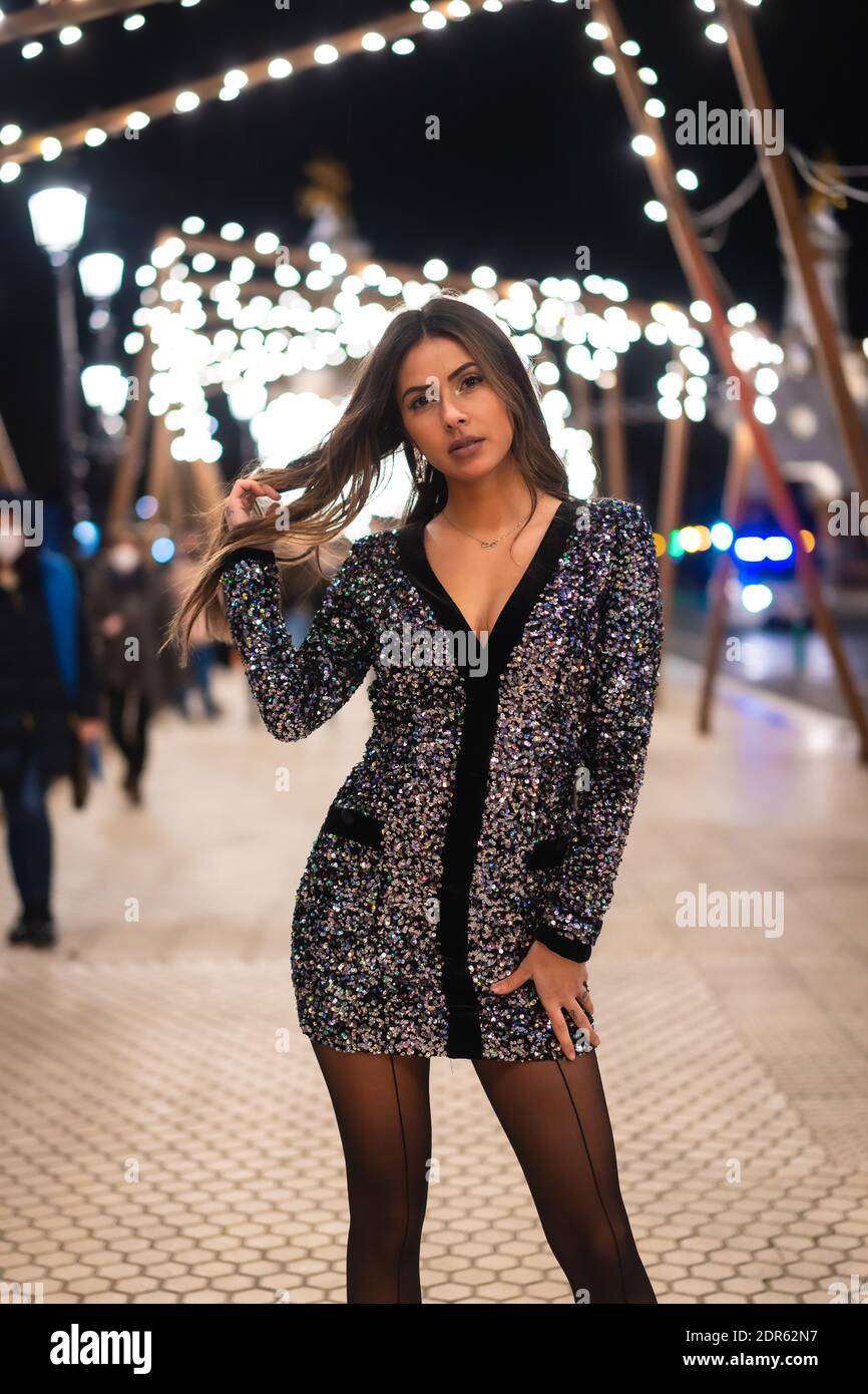 Una donna caucasica alla moda in abito con paillettes in posa nella Città di notte dalle luci di Natale Foto Stock