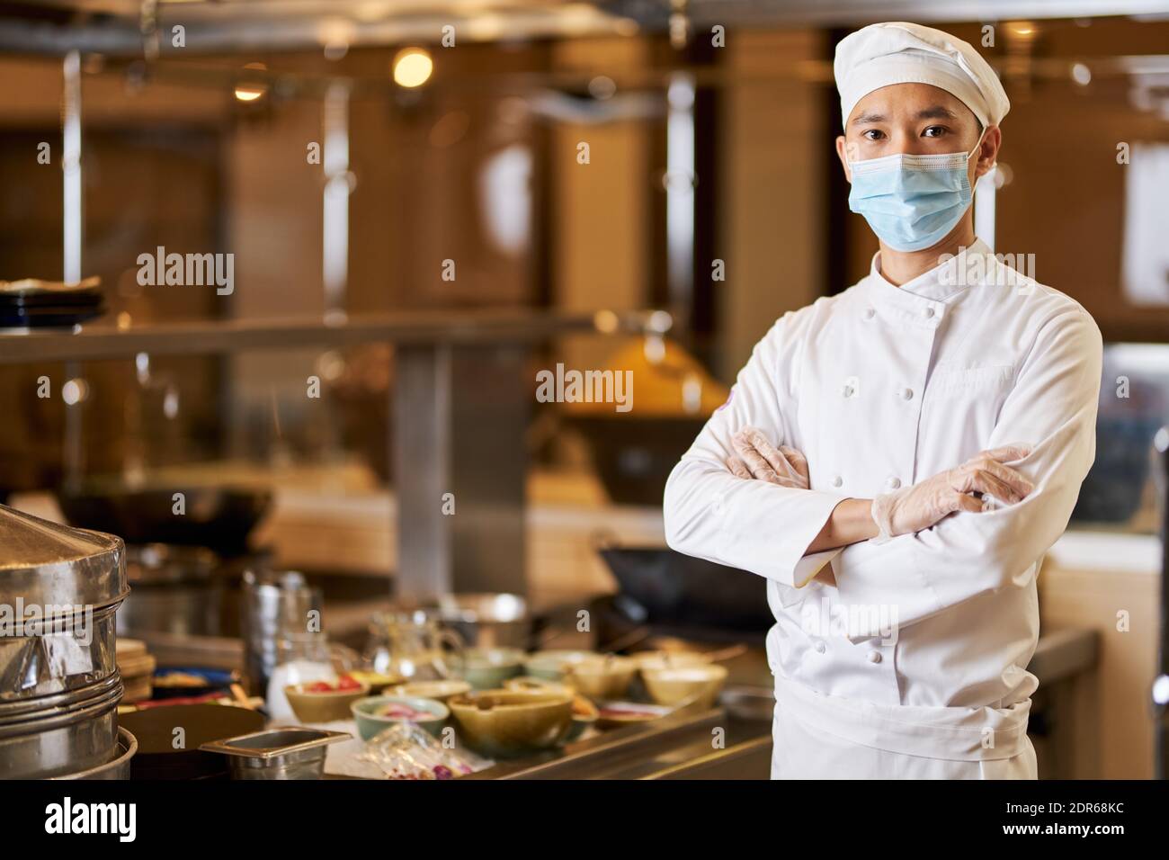 Copia la foto dello spazio di chef asiatico autoassicurato in maschera protettiva in piedi con le braccia incrociate sul petto Foto Stock