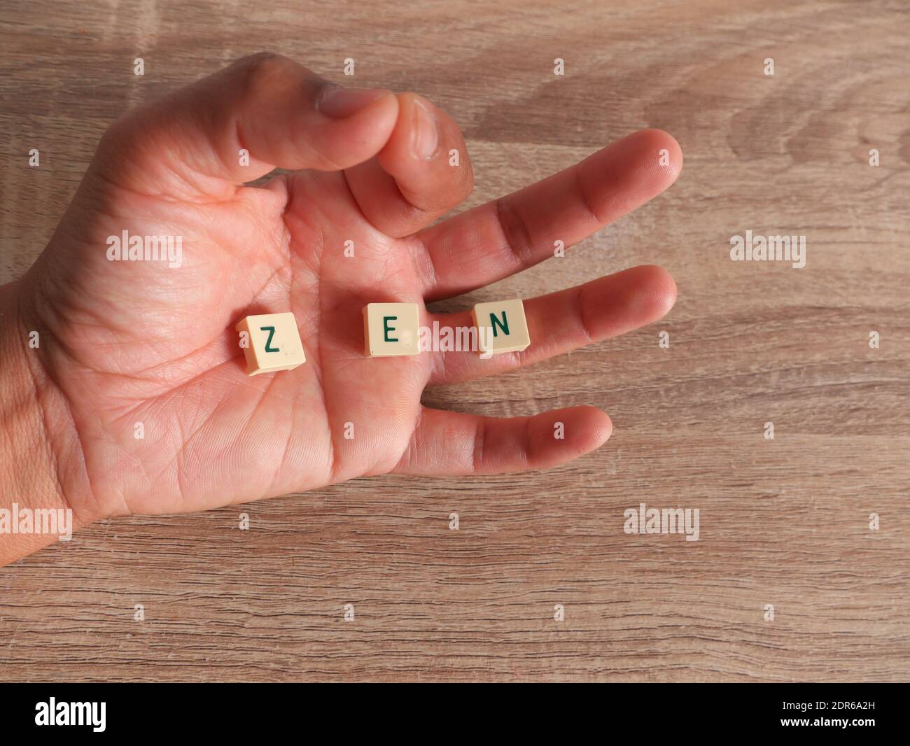 PAROLA ZEN scritta con lettere scrabble all'interno di una mano sopra uno sfondo di legno Foto Stock