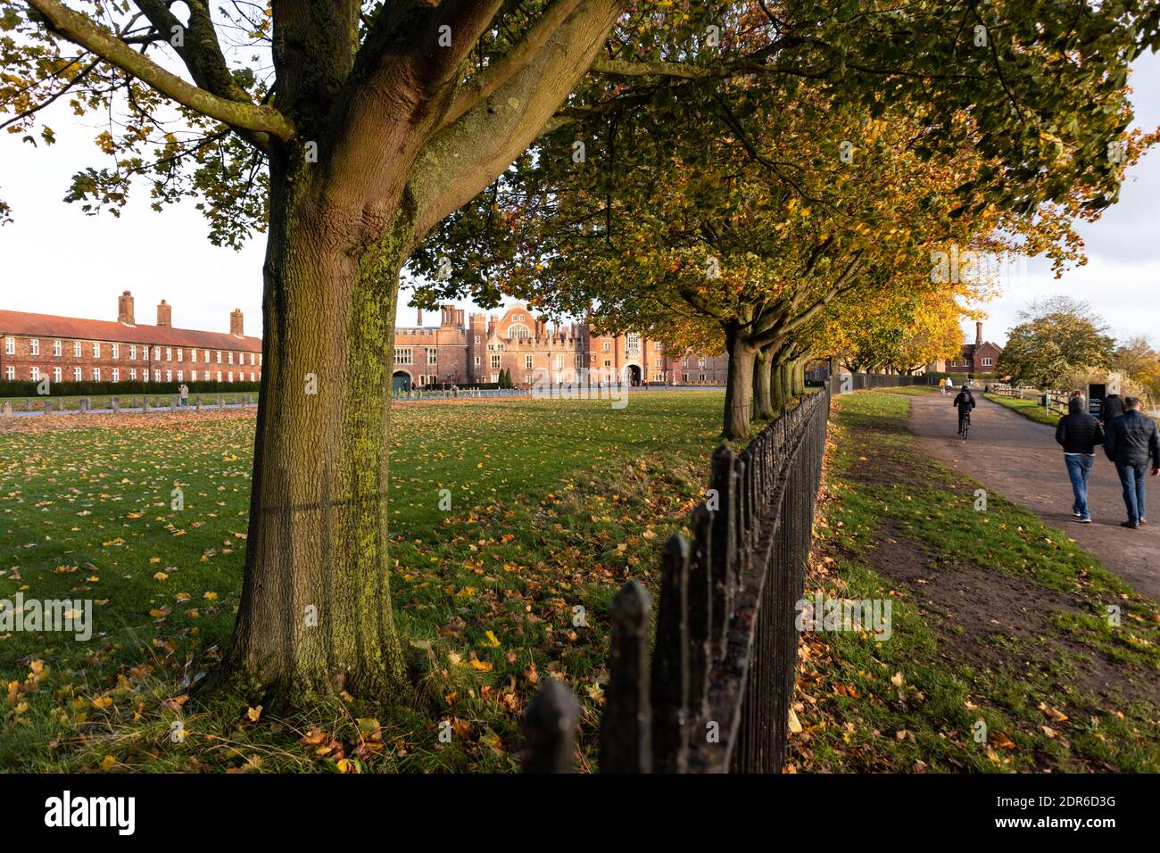 Facciata Tudor rosso brillante dell'Hampton Court Palace visto attraverso Alberi che si trovano lungo il lato del sentiero del fiume Tamigi Foto Stock