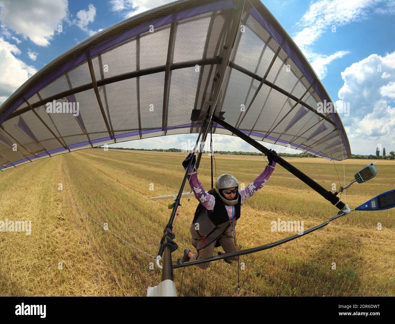 Atterraggio deltaplano. Il pilota atterra un'ala colorata di deltaplano sul campo di grano giallo. Sport estremo. Foto Stock