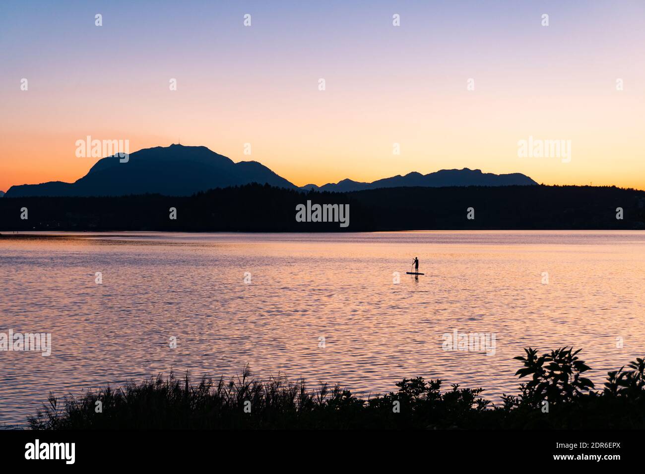 Stand up paddle al lago Faaker vedere in Carinzia, Austria. Splendido tramonto di fronte al monte Dobratsch, sull'idilliaco lago delle Alpi. Foto Stock