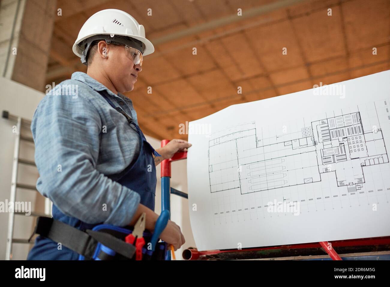 Ritratto ad angolo basso di un ingegnere femminile che ispeziona le planimetrie mentre lavori in cantiere Foto Stock