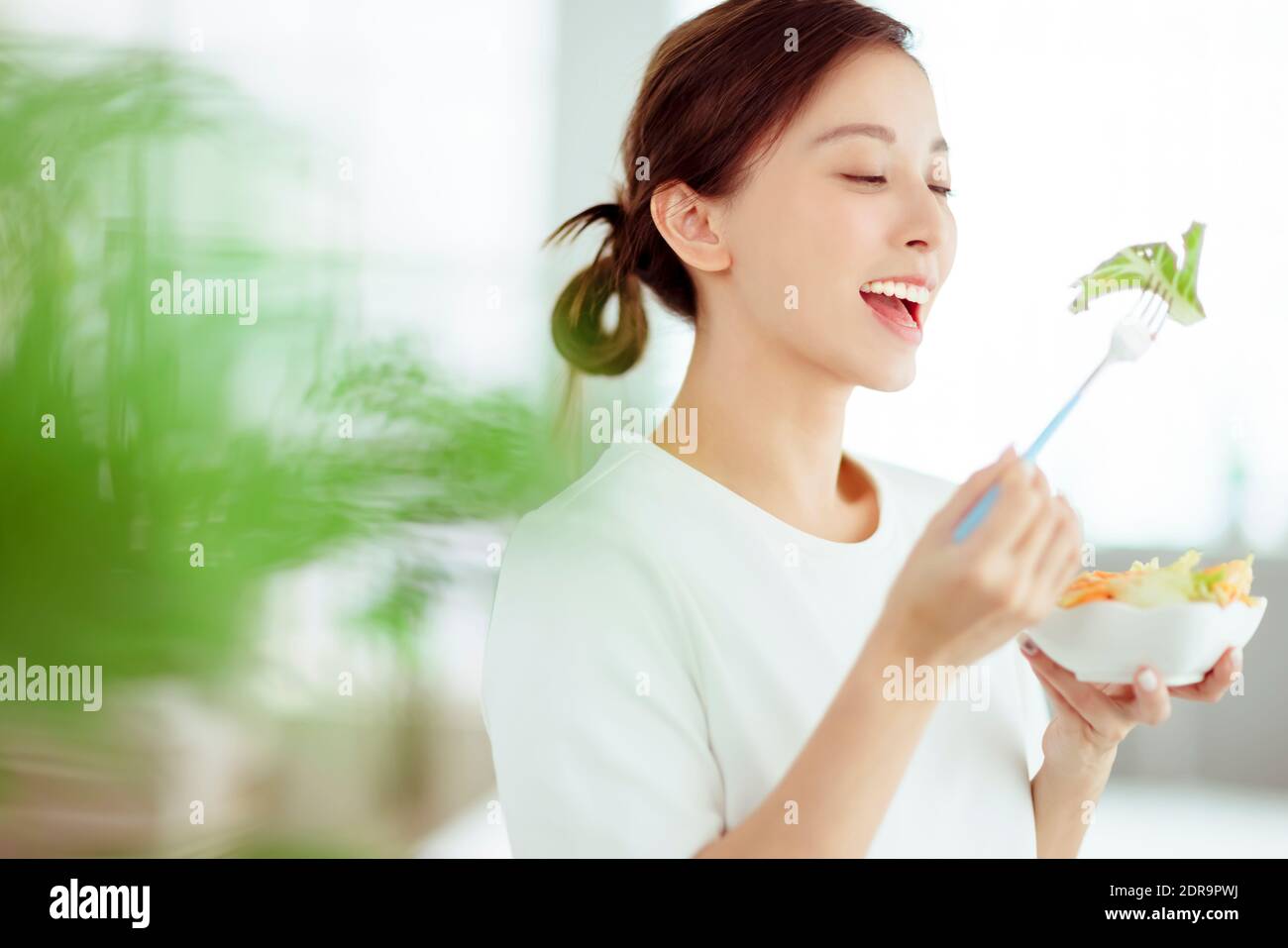 Giovane donna felice che mangia insalata sana a casa Foto Stock