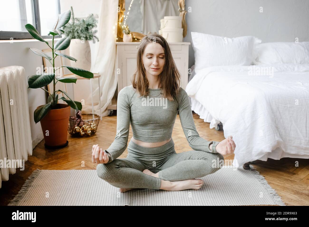 Giovane donna fitness che pratica yoga sul pavimento in camera da letto a casa al mattino. Sport ragazza facendo meditazione in lotus posa esercizio in interni. Salute dell'allenamento Foto Stock