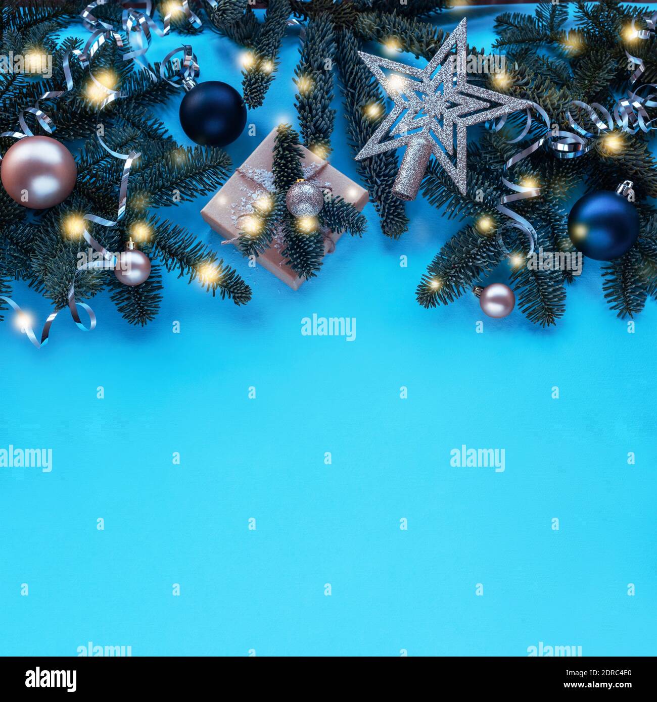 Rami di abete, regalo in scatola e baubles su sfondo blu con luci di Natale. Vista dall'alto, disposizione piatta, spazio per la copia. Foto Stock