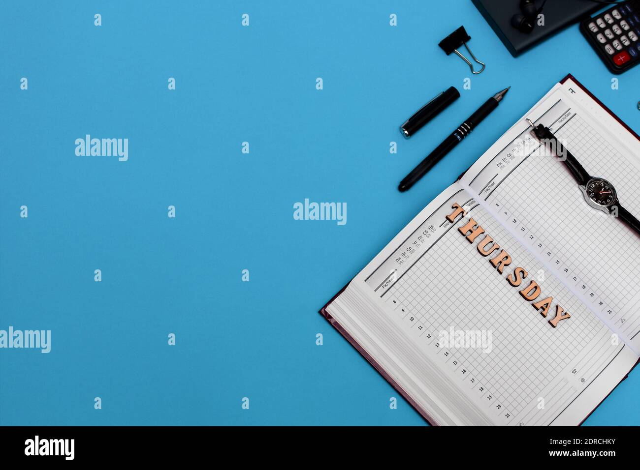 Moderna scrivania da ufficio con notebook, penna e materiali di consumo vuoti. Copiare lo spazio su sfondo blu. Vista dall'alto. Stile di posa piatto. Scritta giovedì Foto Stock