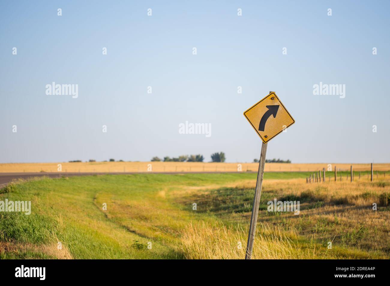 Indicazioni stradali a destra curva avvertimento strada di fronte a verde luminoso e giallo erba sul lato dell'autostrada alberta. Simbolo di avvertenza sulla strada Foto Stock