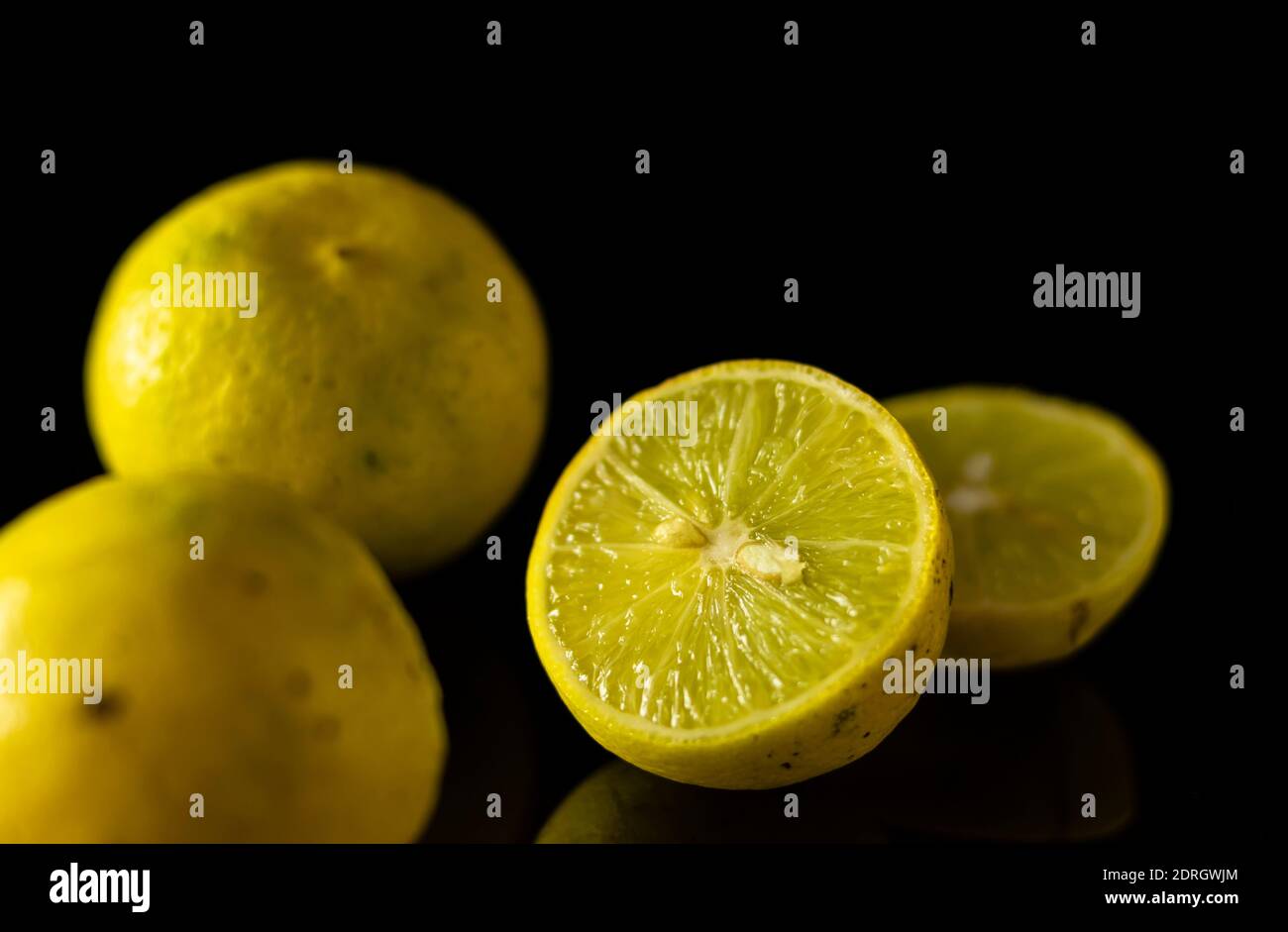 gruppo di limoni e fette su una superficie riflettente e. sfondo nero Foto Stock