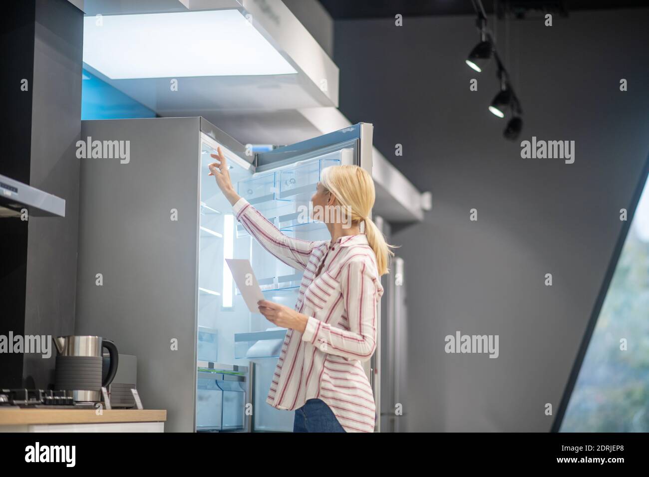 Bionda bella donna choosona frigo in uno showroom Foto Stock