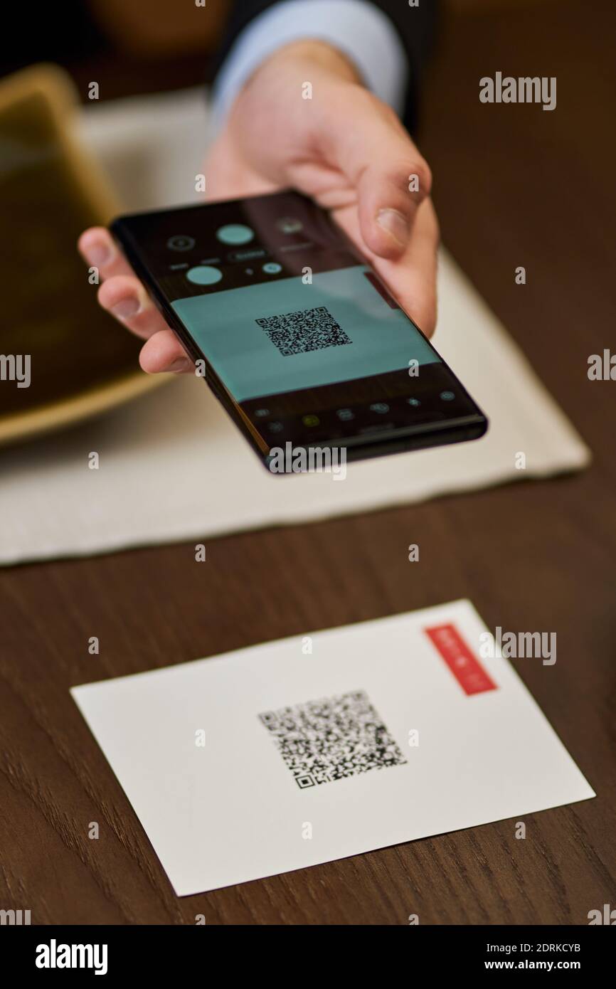 Foto a mano ritagliata con lo smartphone che esegue la scansione di un codice QR su un tavolo da ristorante Foto Stock