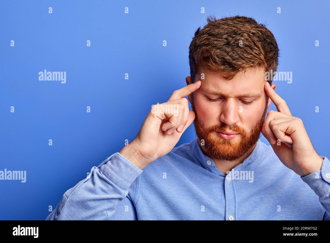ritratto di pensieroso ragazzo caucasico pensando isolato su sfondo blu, stare con gli occhi chiusi, tenendo la testa, concentrato sui pensieri Foto Stock