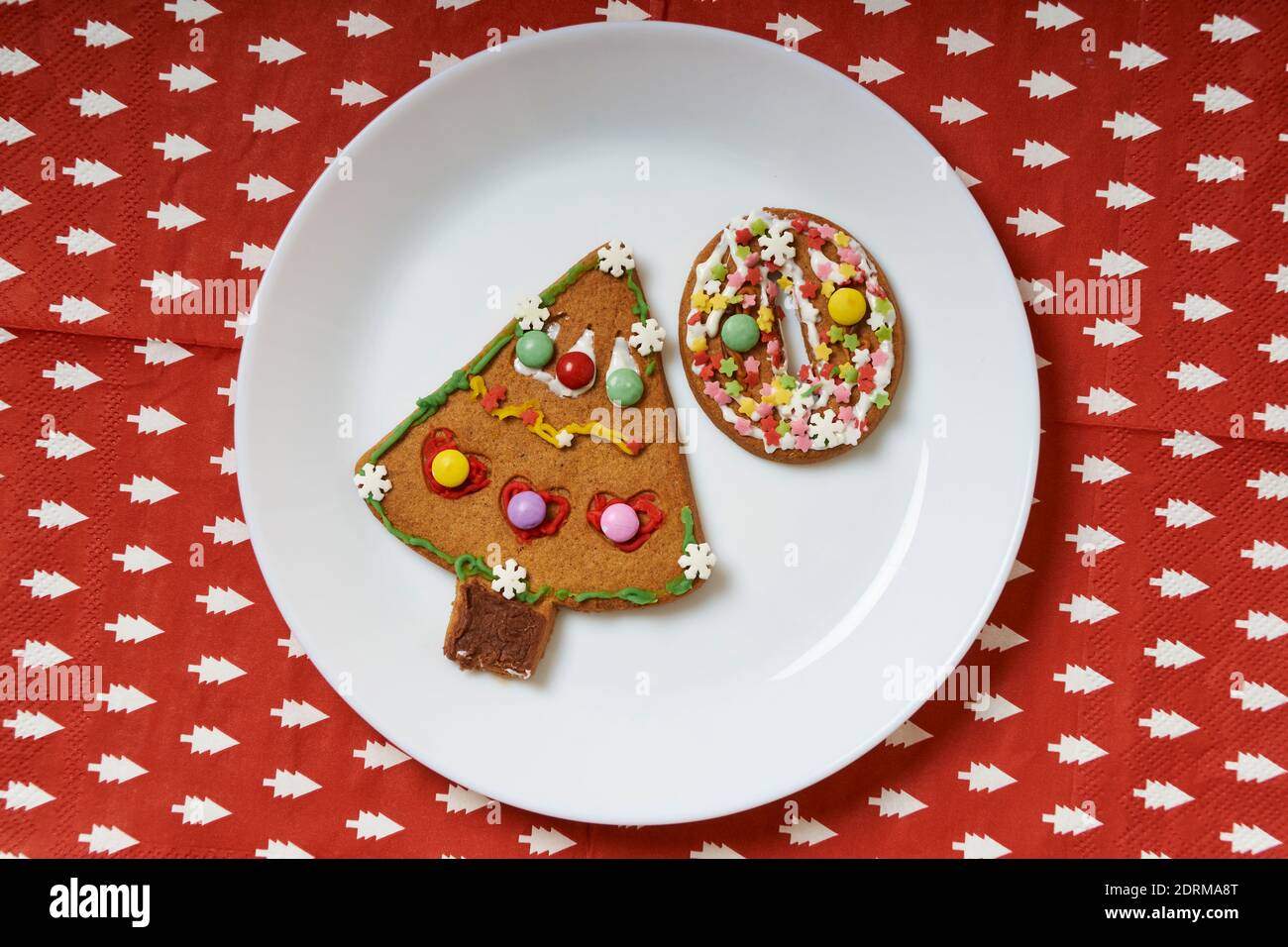 biscotti natalizi decorati con delizie colorate su un tovagliolo rosso con alberi di natale bianchi Foto Stock