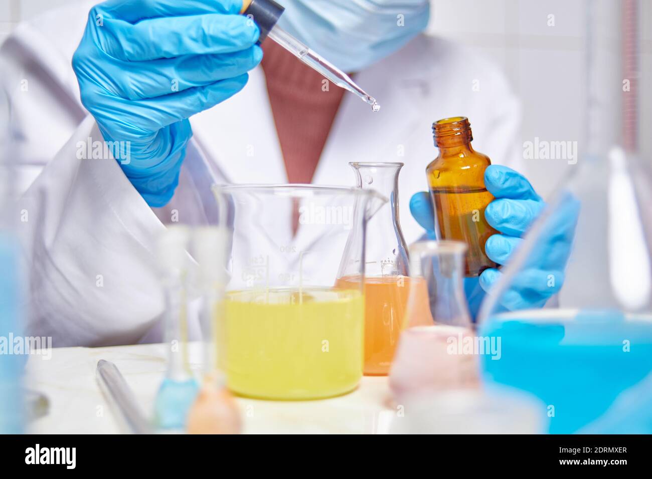 tecnico di laboratorio in camice bianco, guanti blu e maschera facciale che effettua esperimenti e prove in laboratorio con sostanze di colore diverso Foto Stock