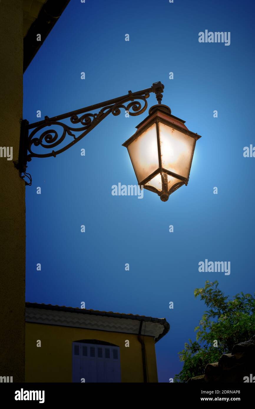 Vecchia lanterna di ferro illuminata sulla parete di notte. Lampada da esterno d'epoca. Foto Stock