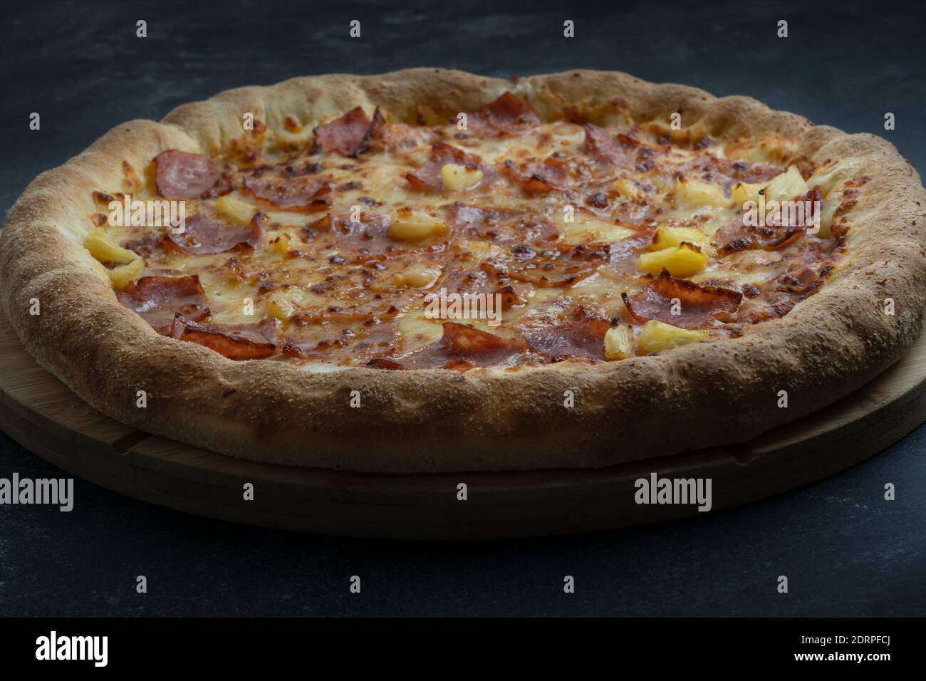 Deliziosa pizza con formaggio, pancetta croccante e ananas su fondo scuro. Foto Stock