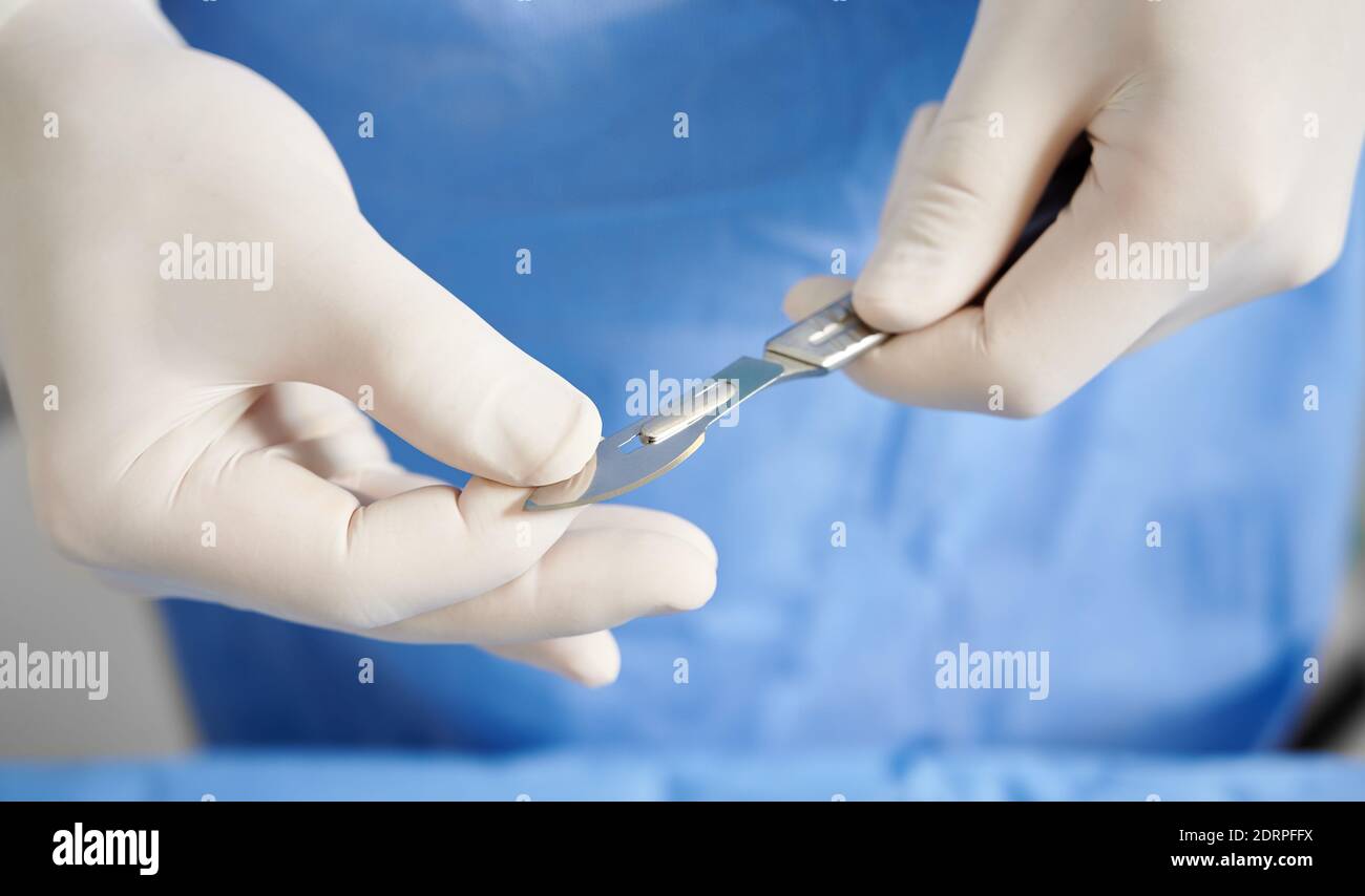 Vista ravvicinata delle mani del medico che si prepara il bisturi per la chirurgia plastica. Chirurgo con strumento medico in acciaio inossidabile in braccio che indossa guanti sterili bianchi. Concetto di chirurgia e medicina. Foto Stock