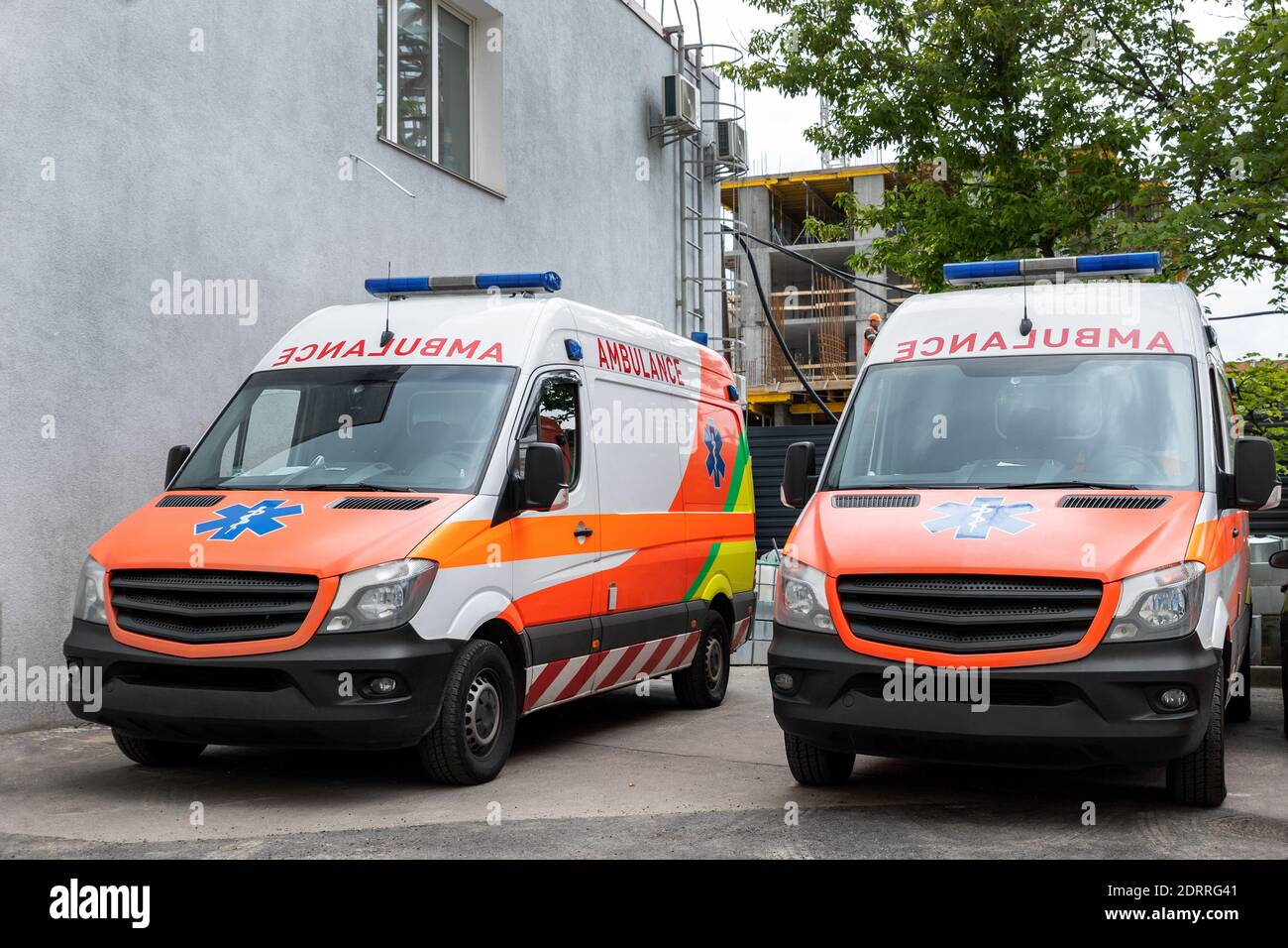 Due moderni furgoni medici di emergenza ambulanza bianco e arancione parcheggiati vicino all'edificio dell'ospedale. Veicoli paramedici sulla strada della città. Assistenza sanitaria e. Foto Stock