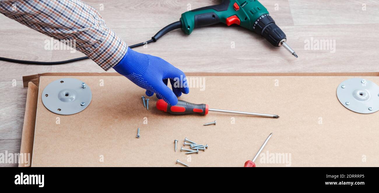 Processo di assemblaggio di mobili con mani maschili in guanti, master raccoglie mobili da tavolo con utensili a cacciavite, strumento di perforazione. In movimento, a casa Foto Stock