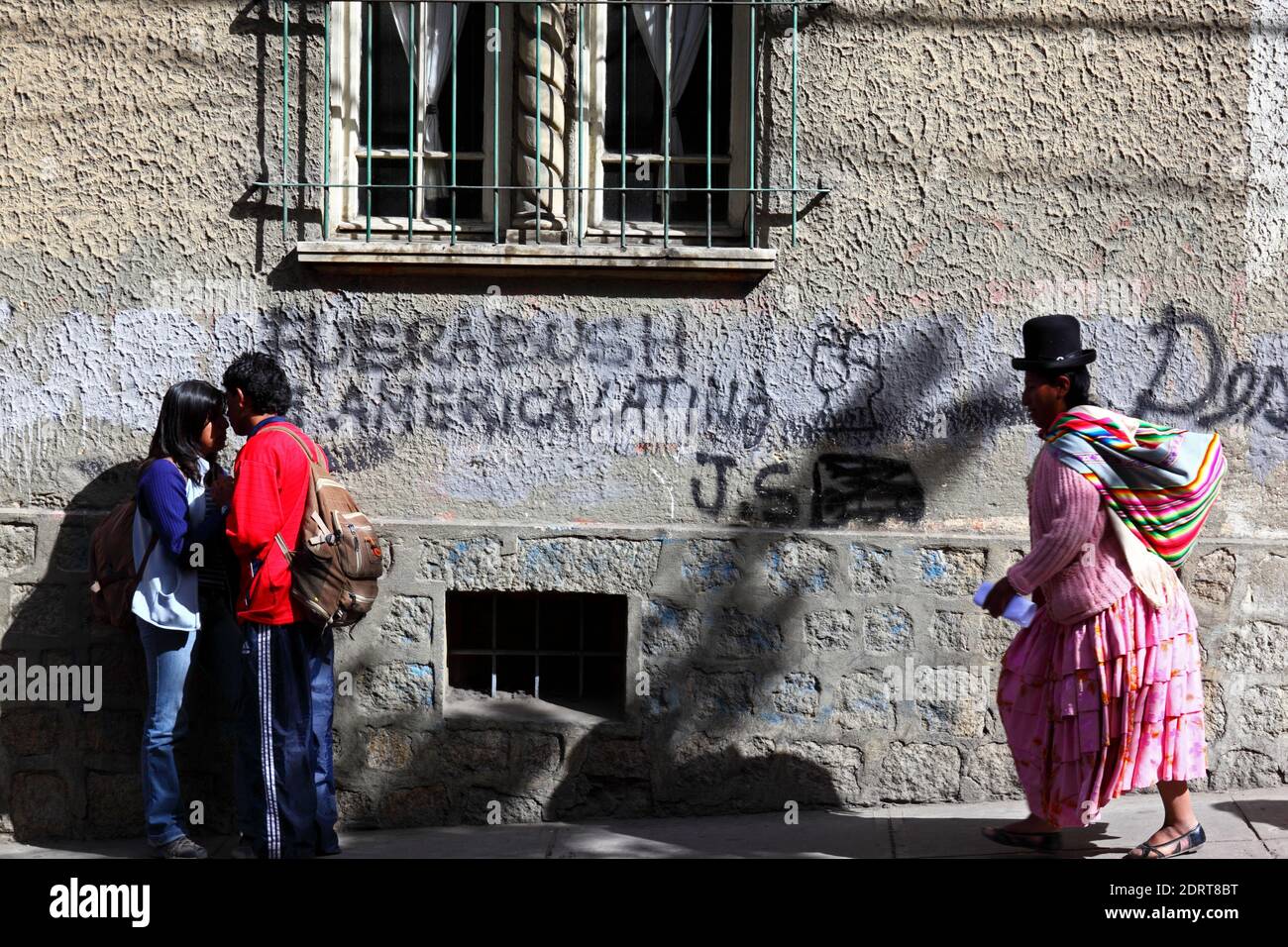 Aymara donna che indossa abito tradizionale a piedi oltre Bush fuori dell'America Latina / Fuera Bush de America Latina graffiti sulla parete, la Paz , Bolivia Foto Stock