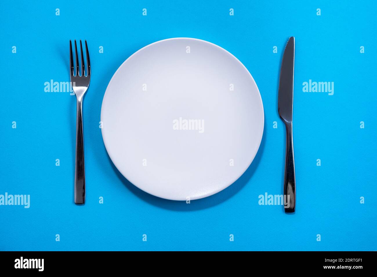 Piatto bianco con utensili su sfondo blu. Messa a fuoco selettiva. Ripresa dall'alto Foto Stock