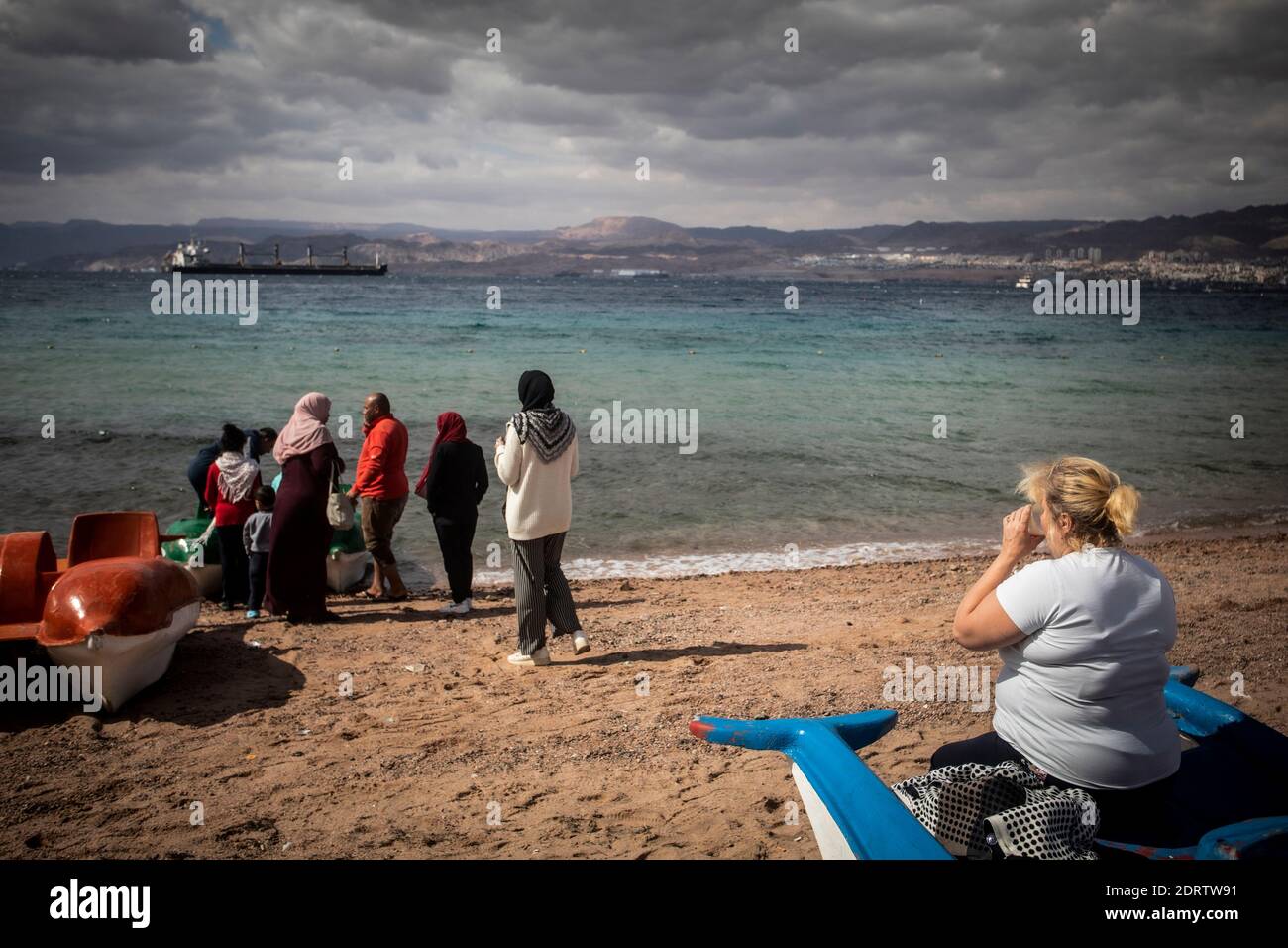 Un turist e una famiglia locale in una spiaggia di Aqaba, Giordania. Dall'altro lato costa di Israele. Foto Stock