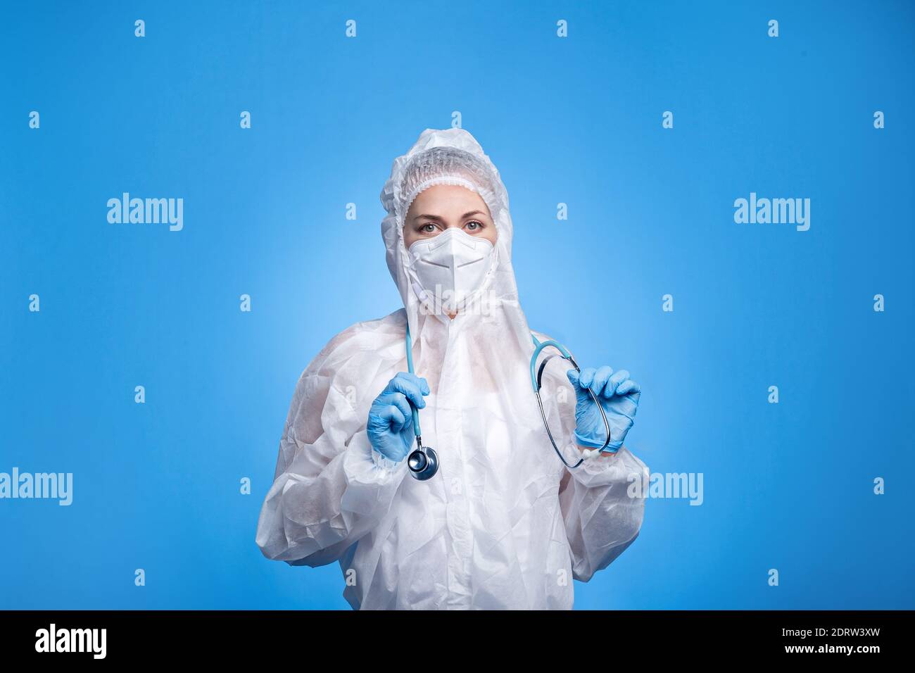 Le mediche femminili indossano la tuta protettiva e tengono lo stetoscopio su sfondo blu. Il medico cura le malattie respiratorie in ospedale Foto Stock