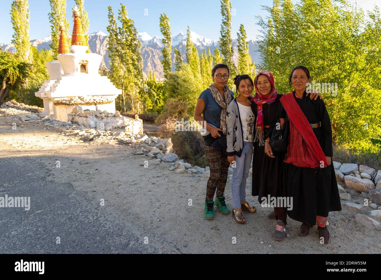 Un gruppo di donne di diverse età e costumi tradizionali si trovano sullo sfondo di cime innevate dell'Himalaya e stupa buddista. Ladakh India Foto Stock