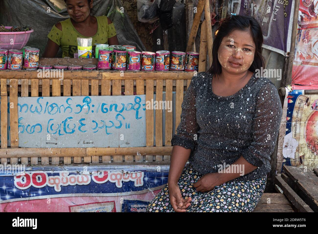 Una donna con trucco tradizionale birmano-Thanaka e una triste espressione sulla sua faccia si siede di fronte ad una bancarella di legno Yangon Myanmar 2019 Foto Stock