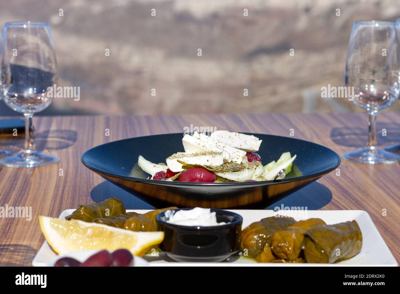 Insalata greca (choriatiki) e foglie d'uva, su un tavolo servito con cucina greca e mediterranea, nel villaggio di Oia, isola di Santorini, Grecia, Europa. Foto Stock