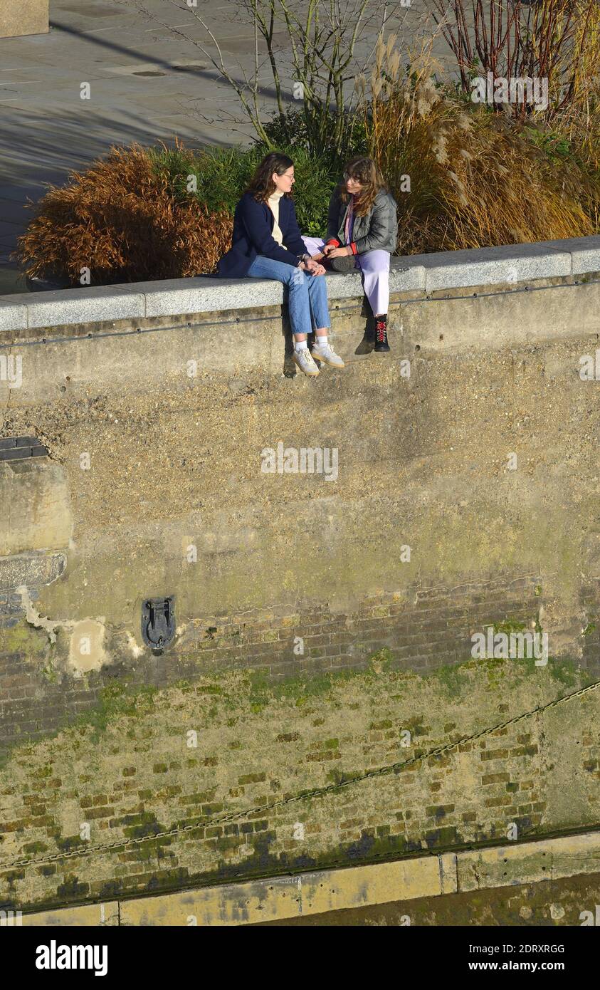 Londra, Inghilterra, Regno Unito. Due giovani donne sedute su un muro sulla riva nord del Tamigi Foto Stock