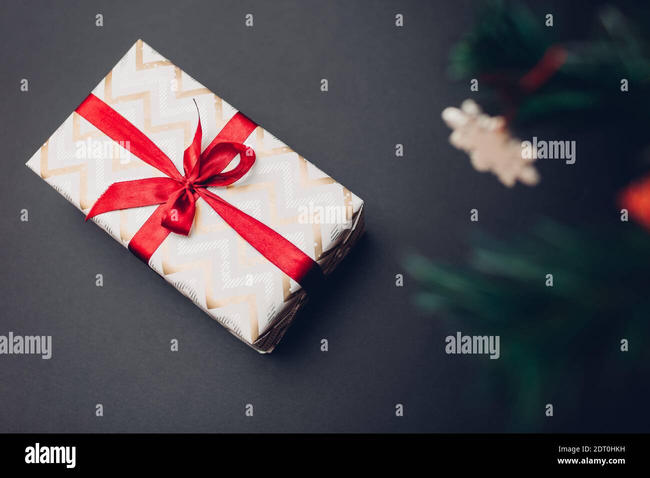 Confezione regalo di Natale e Capodanno avvolta in carta festiva e decorata con nastro rosso con arco su sfondo nero. Presente messo sotto albero di Natale Foto Stock