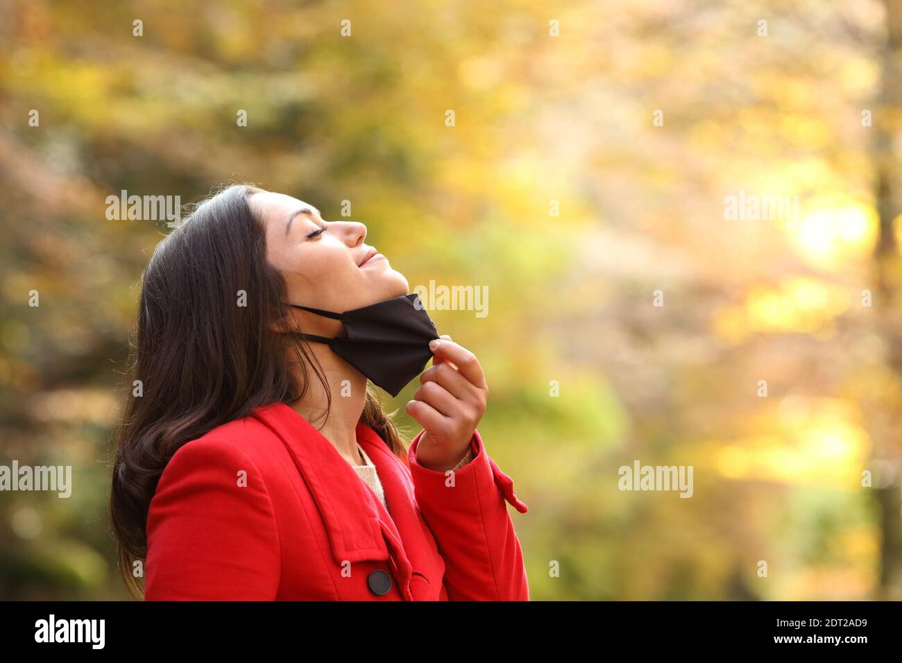 Profilo di una donna che prende la maschera protettiva per respirare aria fresca in un parco in tempi brevi Foto Stock