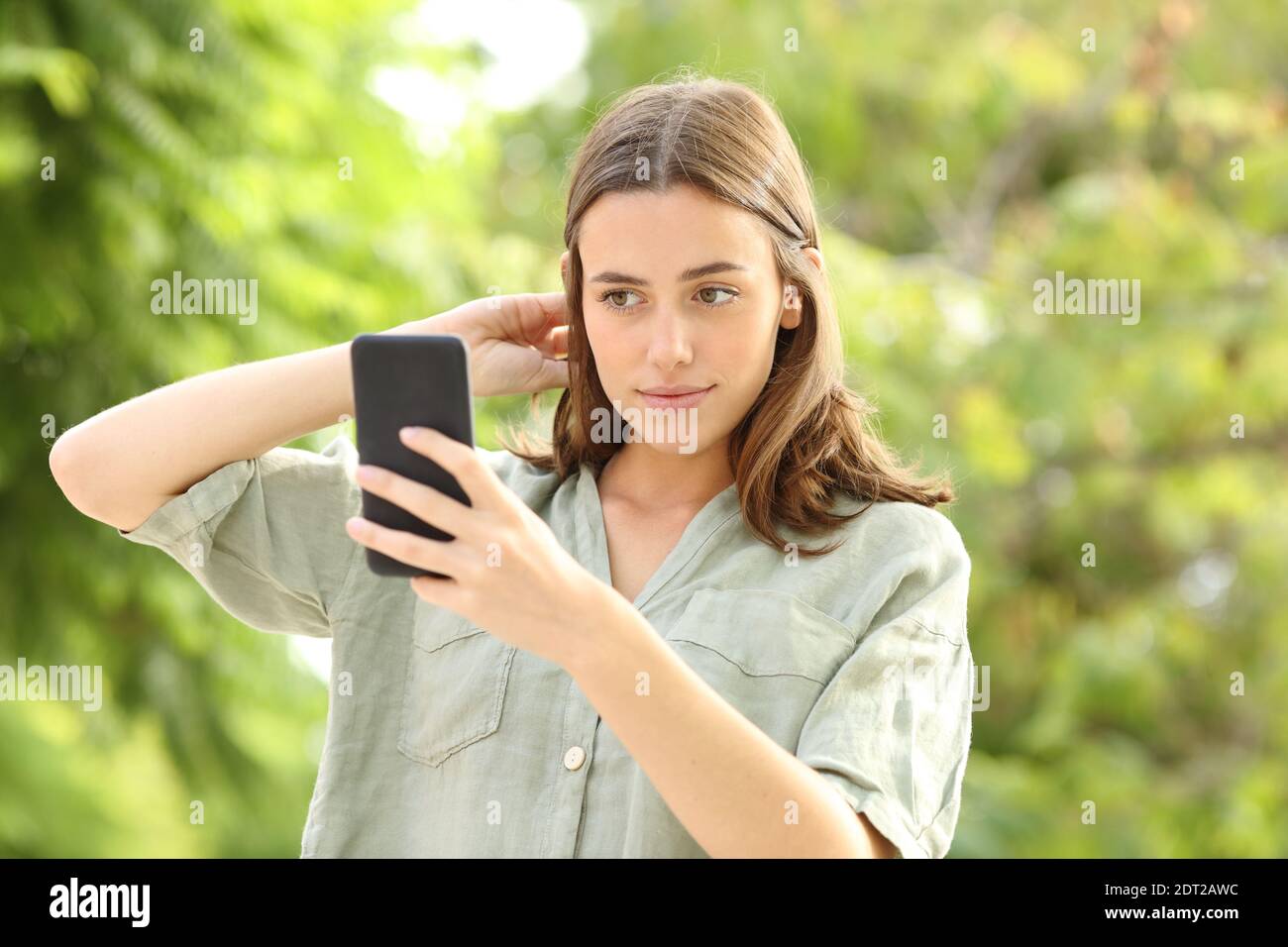 Donna che pettina i capelli usando lo smartphone come specchio in un parcheggio Foto Stock