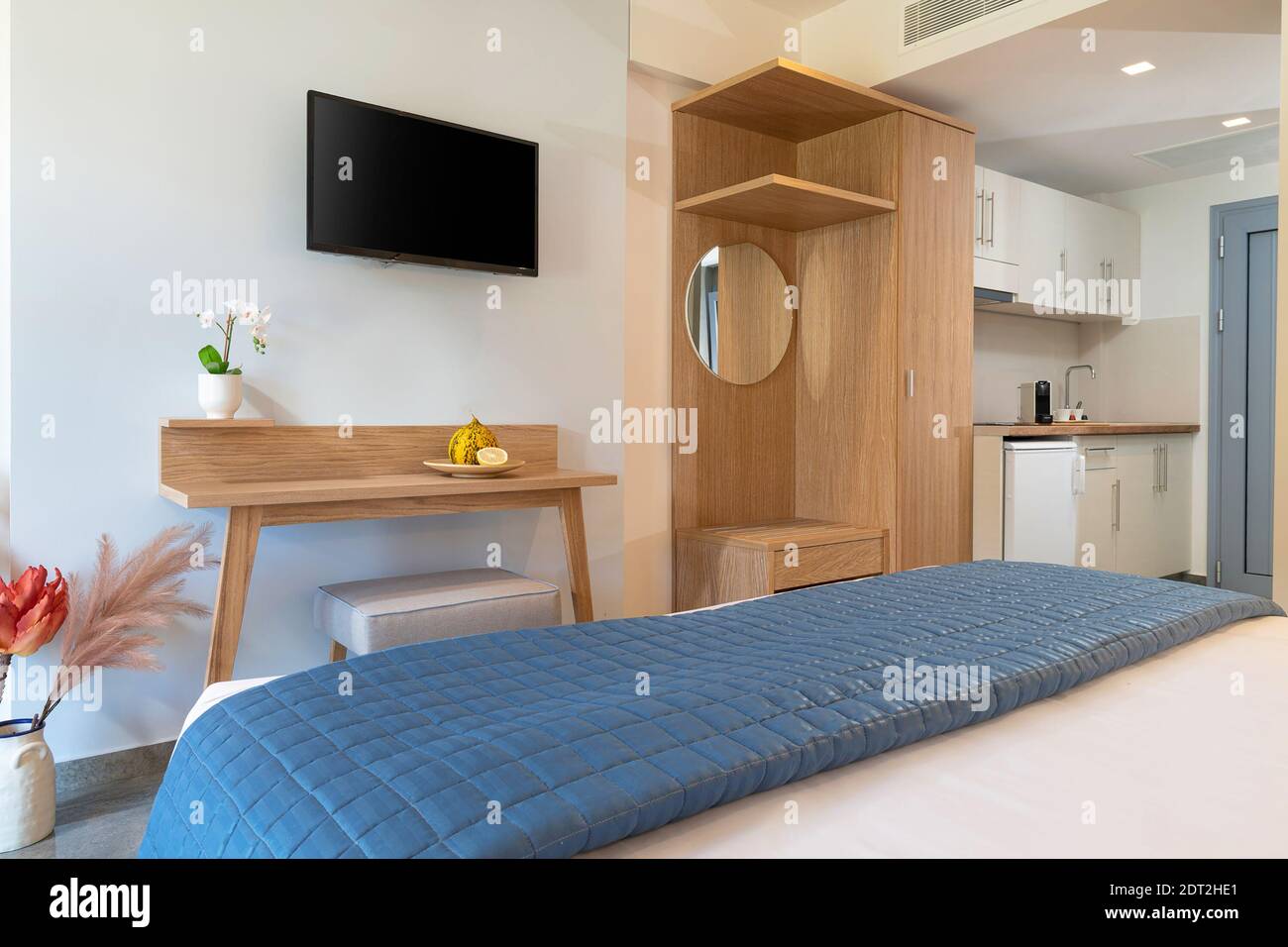 Interni in stile moderno di un piccolo monolocale. Camera d'albergo con cucina bianca, camera da letto blu, armadio in legno di pino, TV a schermo piatto in camera singola Foto Stock