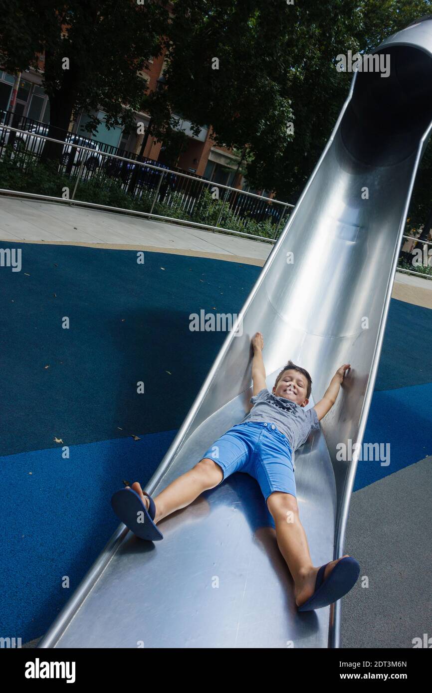 Un ragazzo divertente che gioca sullo scivolo del tunnel nel parco pubblico Foto Stock