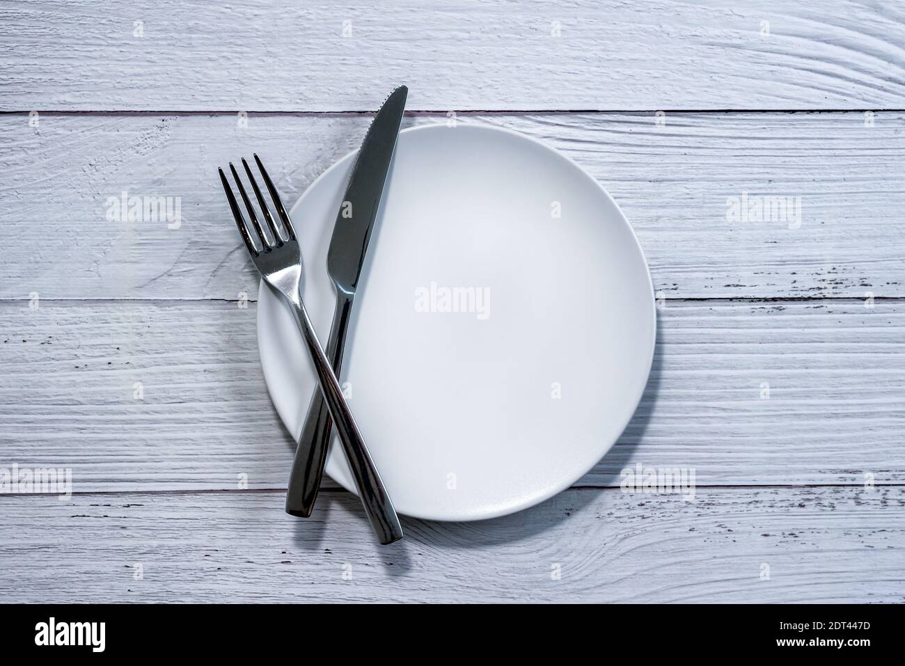 Forchetta e coltello su una piastra bianca vuota, sfondo di tavola di legno bianco Foto Stock