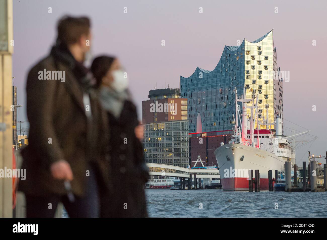 SpaziergŠnger sind bei Sonnenuntergang an den LandungsbrŸcken unterwegs. Im Hintergrund ist die Elbphilharmonie und das Museumsschiff Cap San Diego im Foto Stock