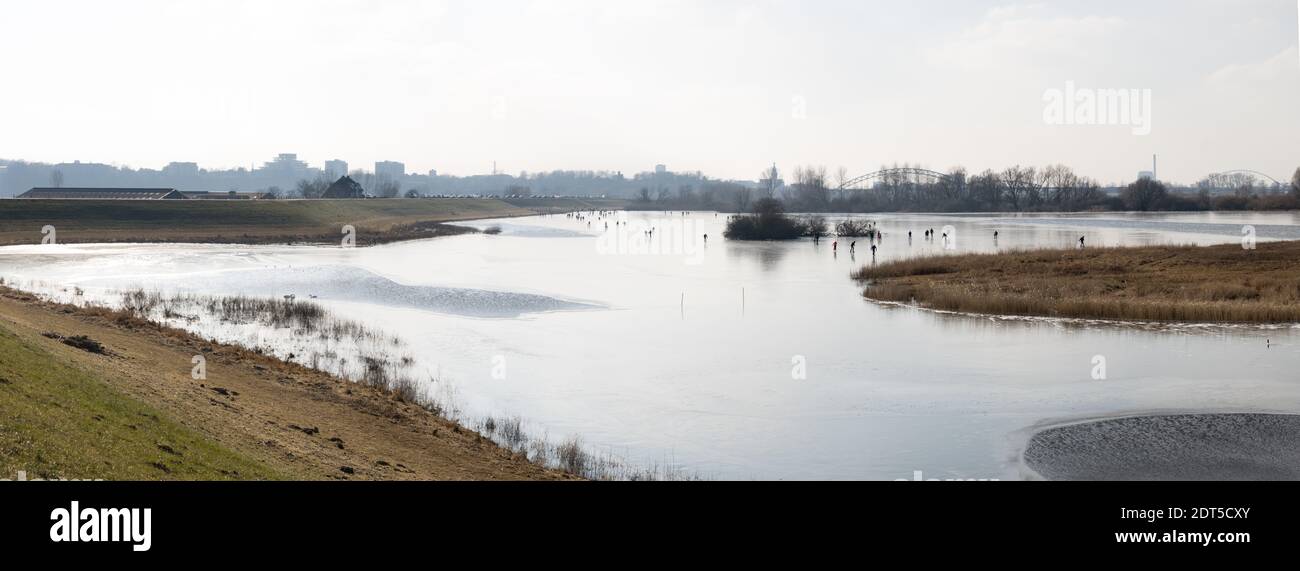 Braccio laterale del fiume Reno vicino Nijmegen in inverno con ghiacciatori sul ghiaccio e il paesaggio urbano in lontananza Foto Stock