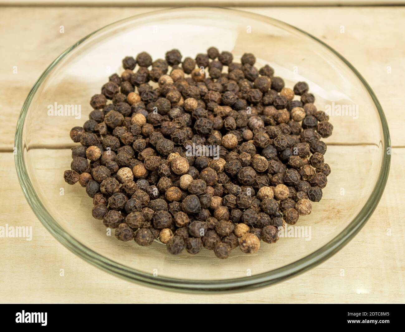 Spezia pepe i piselli neri in un piatto di vetro su a. sfondo di legno Foto Stock