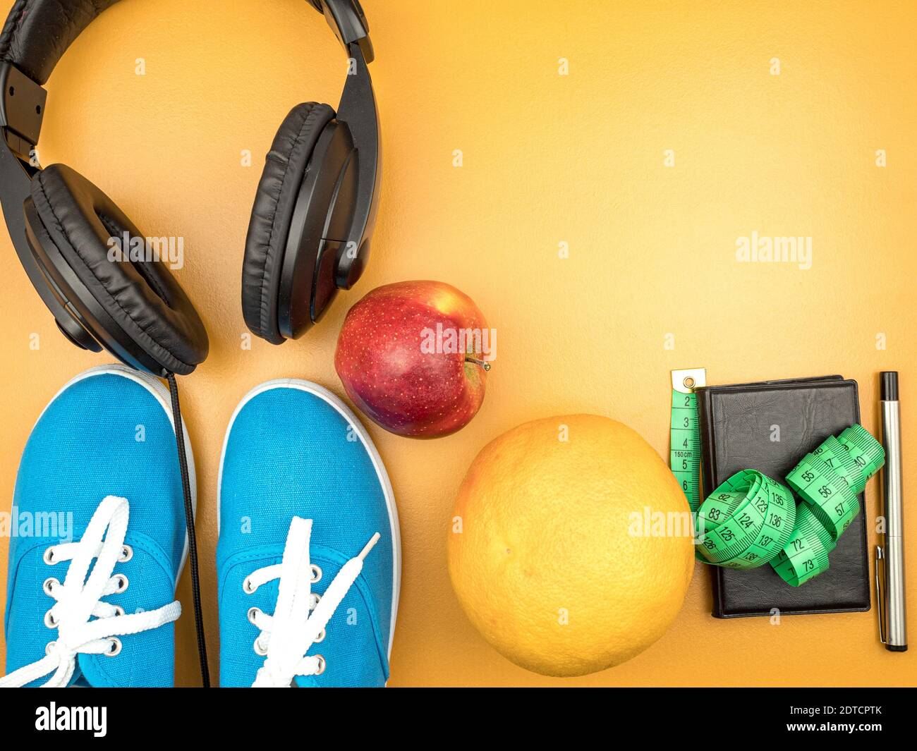 Notebook con frutta e sneakers vista dall'alto. Cuffie per lo sport. Cornice per il progettista. Dieta, sport, autodisciplina. Foto Stock