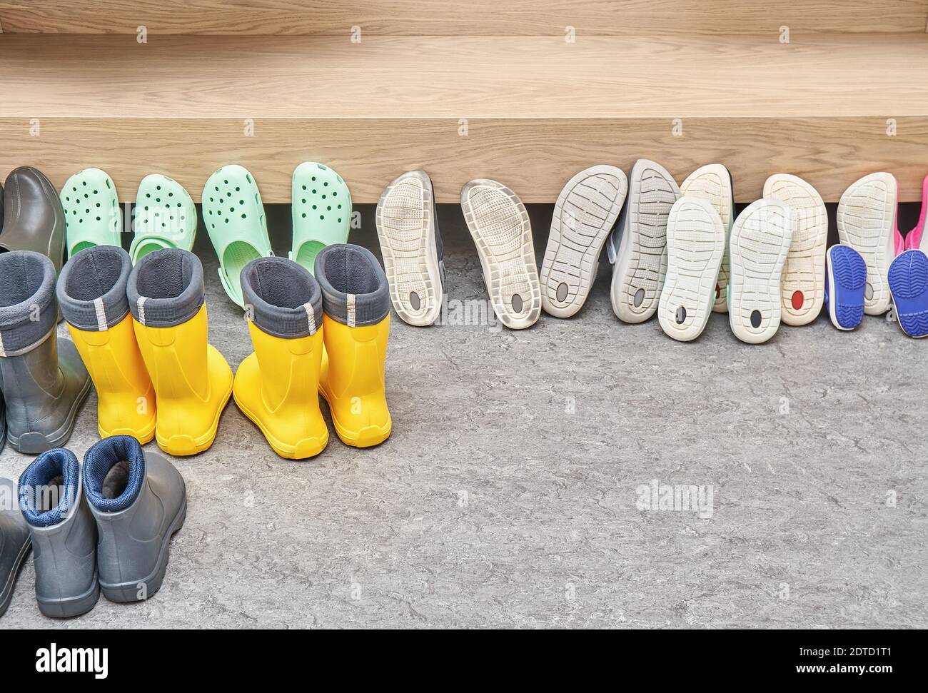 Collezione di scarpe e stivali in piedi vicino a mobili contemporanei in legno compensato chiaro e impiallacciatura di quercia su pavimento grigio Foto Stock