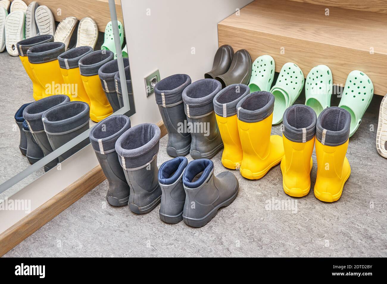 Collezione di scarpe e stivali in piedi vicino a mobili contemporanei in legno compensato chiaro e impiallacciatura di quercia su pavimento grigio Foto Stock