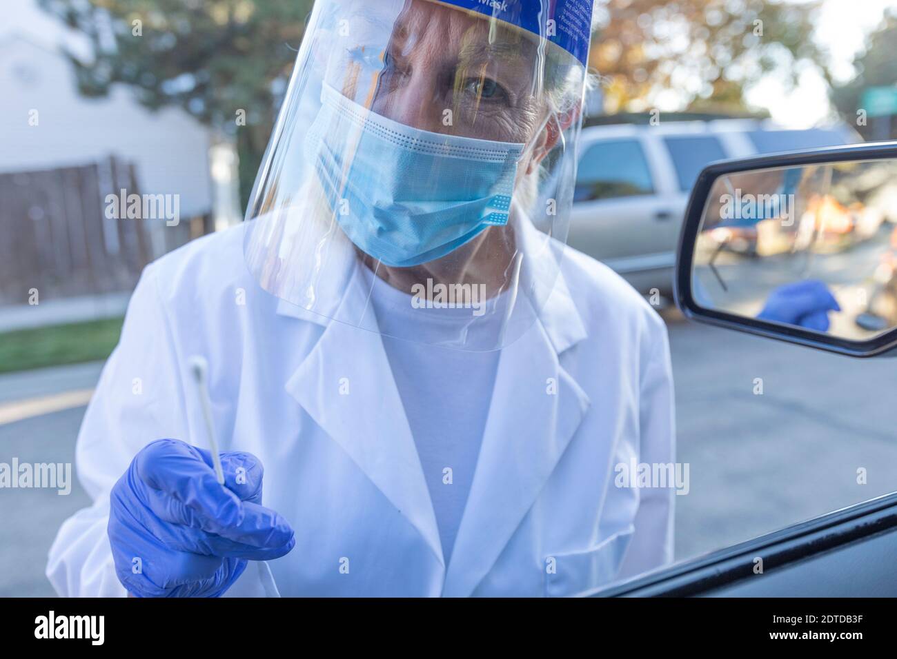 Personale medico femminile in abbigliamento protettivo che si avvicina auto con coronavirus test con tampone Foto Stock