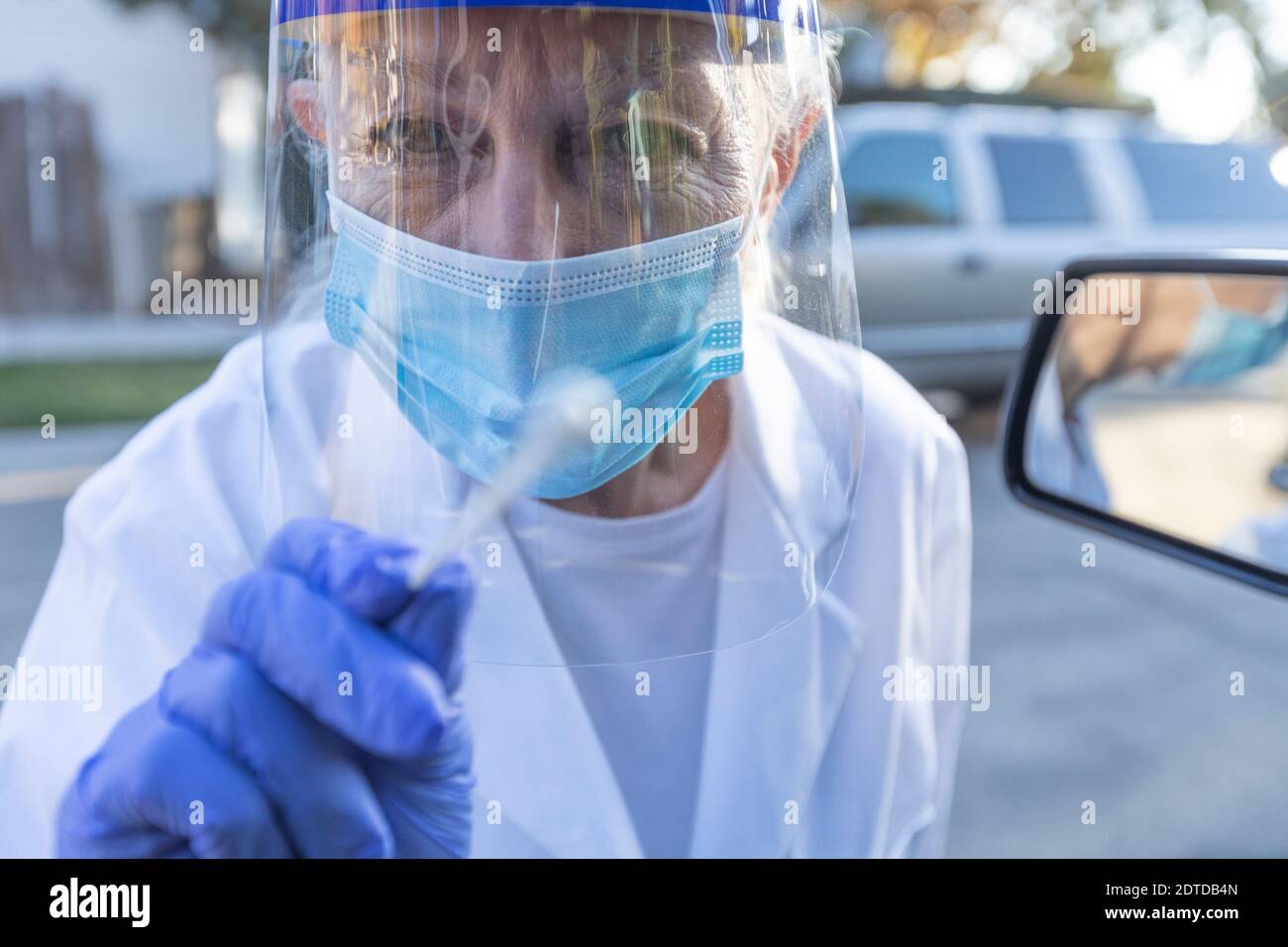 Personale medico femminile in abbigliamento protettivo che si avvicina auto con coronavirus test con tampone Foto Stock