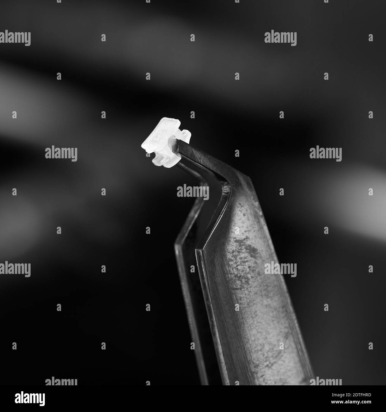 Primo piano dello strumento dentale che tiene la staffa ortodontica. Utensili dentali per il fissaggio di bretelle a denti isolati su sfondo nero. Concetto di odontoiatria, strumenti medici e trattamento ortodontico. Foto Stock